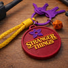 Stranger Things themed keychain with purple keys and orange dice on wooden surface
