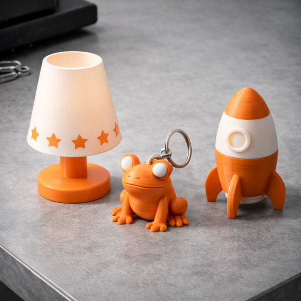 Set of small lamp, frog-shaped keychain, and rocket-shaped object on a gray surface